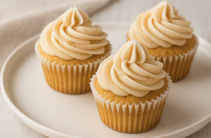 Three cupcakes on a white plate, topped with maple frosting in a swirl pattern