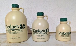 Three Dodge's Sugar Shack maple syrup jugs--half gallon, quart and pint sizes--displayed side by side on a light background.