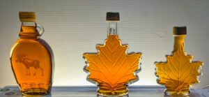 Backlit glass bottles filled with maple syrup feating a moose design and two maple leaf-shaped bottles glowing with amber color.